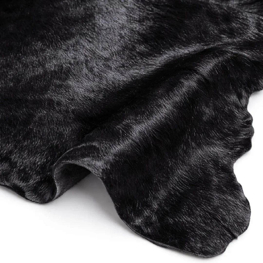 Black cowhide leather rug with natural texture and wavy edge on white background