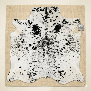 Black and white cowhide leather rug with spotted pattern on a beige woven mat